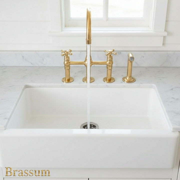White kitchen sink with gold faucet and handles on a marble countertop.