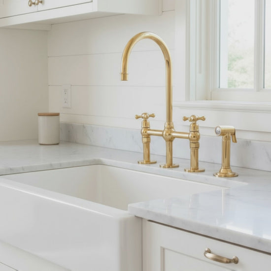 Classic farmhouse-style solid brass bridge faucet with running water over a white apron sink and granite countertop.