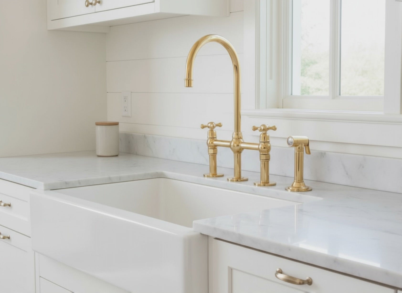 Classic farmhouse-style solid brass bridge faucet with running water over a white apron sink and granite countertop.